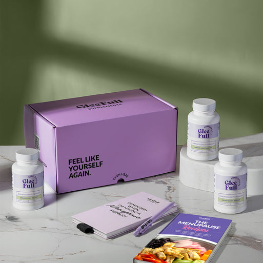 A product bundle display for GleeFull Supplements on a marble surface against a green background. The layout includes a large purple shipping box featuring the slogan 'FEEL LIKE YOURSELF AGAIN.', three white bottles of Meno Joint Relief, a purple branded pen, a matching notepad that reads 'REMINDERS WHEN I'M HAVING A MENOPAUSE MOMENT', and a recipe booklet titled 'THE MENOPAUSE Recipes'
