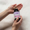 A person holds a dark amber GleeFull Over 30 Hormone Support Plus bottle with tan capsules in their open palm, against a soft cream blanket. Label reads 'Promotes Hormonal Balance'.