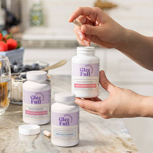 GleeFull Over 30 Hormone Support, Meno Belly Flusher, and Meno-Shred Fat Burner bottles on a marble countertop in a kitchen setting.