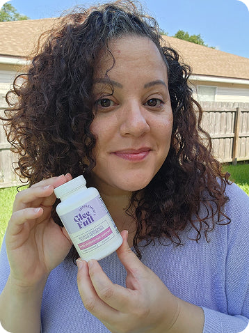 A woman with curly brown hair holds a white bottle of 'GleeFull' dietary supplements in front of a wooden fence and house in an outdoor backyard setting.