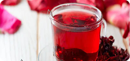 Glass mug filled with red tea or juice, surrounded by fruit slices on a white surface.